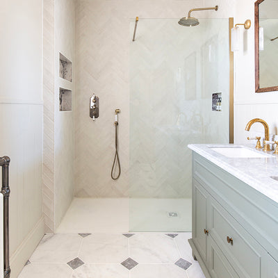 Elegant bathroom with a glass-enclosed shower, brass fixtures, and a herringbone-patterned wall with Parisian Manoir Tumble Cabochon floor. A mint green vanity with marble top adds a soothing tone.
