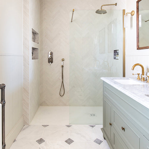 Elegant bathroom with a glass-enclosed shower, brass fixtures, and a herringbone-patterned wall with Parisian Manoir Tumble Cabochon floor. A mint green vanity with marble top adds a soothing tone.