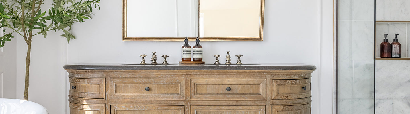 Elegant bathroom with Carrara Bianco marble tiles with a rustic wooden vanity, large mirror, marble shower, and bright window. A potted plant and basket add natural elements. Serene ambiance.
