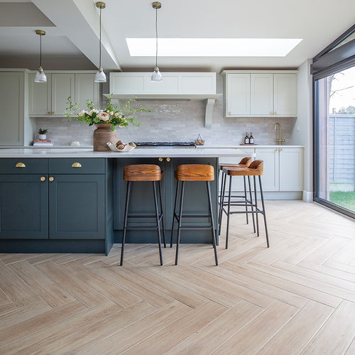 A kitchen with a bar and stools with Falmouth Sandy Oak herringbone floor